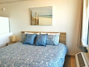 A bedroom with a bed, a wall-mounted painting, and a window with curtains.