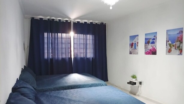 Een slaapkamer met twee bedden, een raam met gordijnen, een kroonluchter en drie aan de muur bevestigde afbeeldingen.