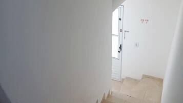 Uma escadaria com azulejos bege que leva a uma porta com moldura branca e uma pequena janela.