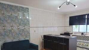 Een moderne keuken met witte tegels, een blauwe bank en een eethoek met stoelen.