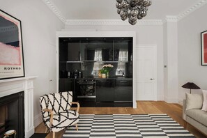 Ein modernes Wohnzimmer mit Kamin, einem schwarz-weißen Streifen Teppich, einer schwarzen Küche mit Glastür und einer Chandelier.