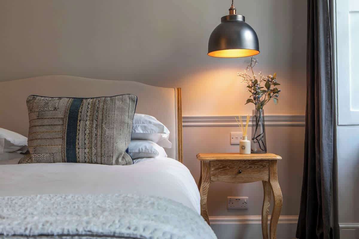 A neatly made bed with a patterned pillow, a bedside table with a vase of flowers, and a hanging lamp.