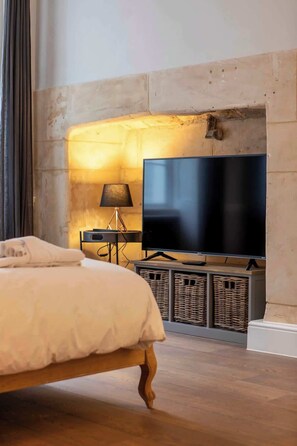 Een slaapkamer met een bed, een televisie op een standaard, een lamp en een open haard.