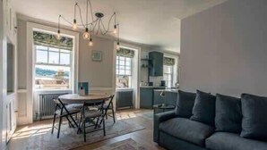 A modern living room with a dark sofa, a round dining table with chairs, and a chandelier. - The Paragon Abode Bath Central Period Apartment (Bath)