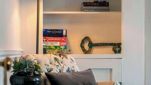 A cozy living room with a floral sofa, a small side table with a plant, a bookshelf with books, and a decorative wall hanging. - The Paragon Abode Bath Central Period Apartment (Bath)