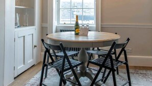 A dining area with a round table, black chairs, a bottle of wine, a menu, and a window with a view. - The Paragon Abode Bath Central Period Apartment (Bath)