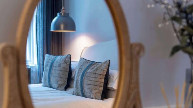 A bedroom with a bed, pillows, a bedside lamp, and a mirror. - The Paragon Abode Bath Central Period Apartment (Bath)