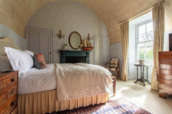 Ein Schlafzimmer mit Bett, Schminktisch, Kommode und einem Fenster mit Vorhängen.