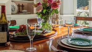 Une table à manger dressée avec des assiettes, des verres et une bouteille, agrémentée d’un vase de fleurs et offrant une vue sur la fenêtre.