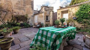 Un bâtiment en pierre avec une table recouverte d’une nappe à carreaux, des plantes en pot et un décor extérieur rustique.
