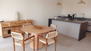 A modern kitchen with a round wooden table, wicker chairs, a built-in island with a sink, and pendant lighting.