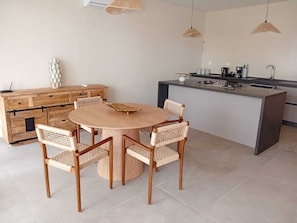 A modern kitchen with a round wooden table, wicker chairs, a built-in island with a sink, and pendant lighting.