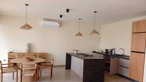 A modern kitchen with a dining area, featuring a round table, chairs, pendant lights, and a built-in island with a stove.