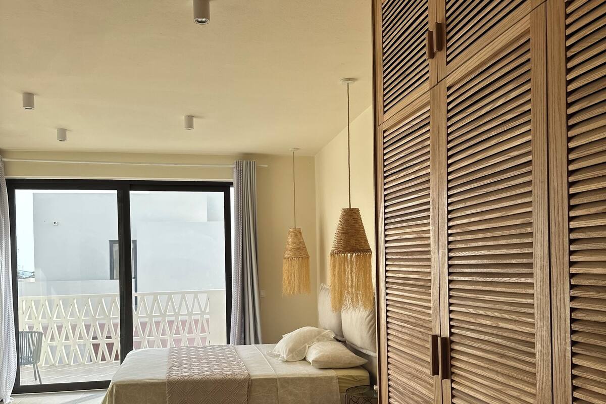 A bedroom with a bed, a balcony, and a wooden wardrobe.
