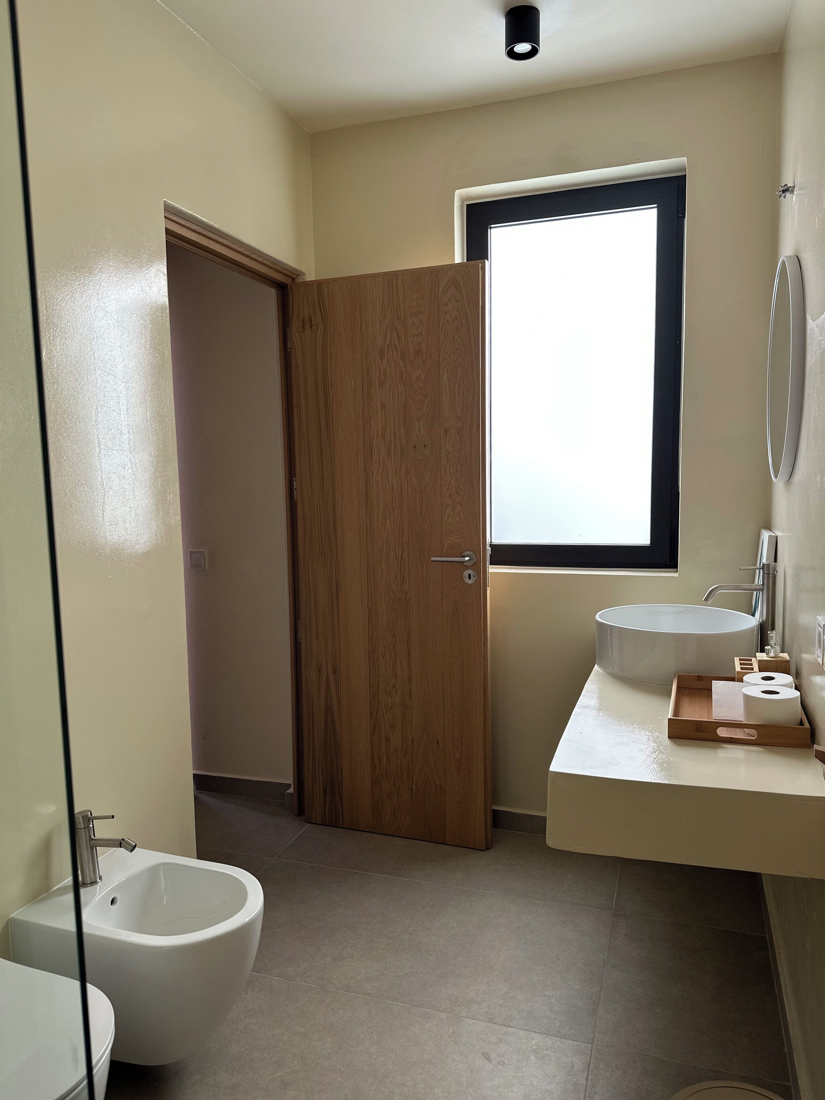 A bathroom with a bidet, toilet, sink, and a wooden door.