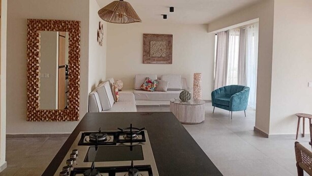 A modern kitchen with a central island, a dining area with a table, a sofa, and a blue armchair.