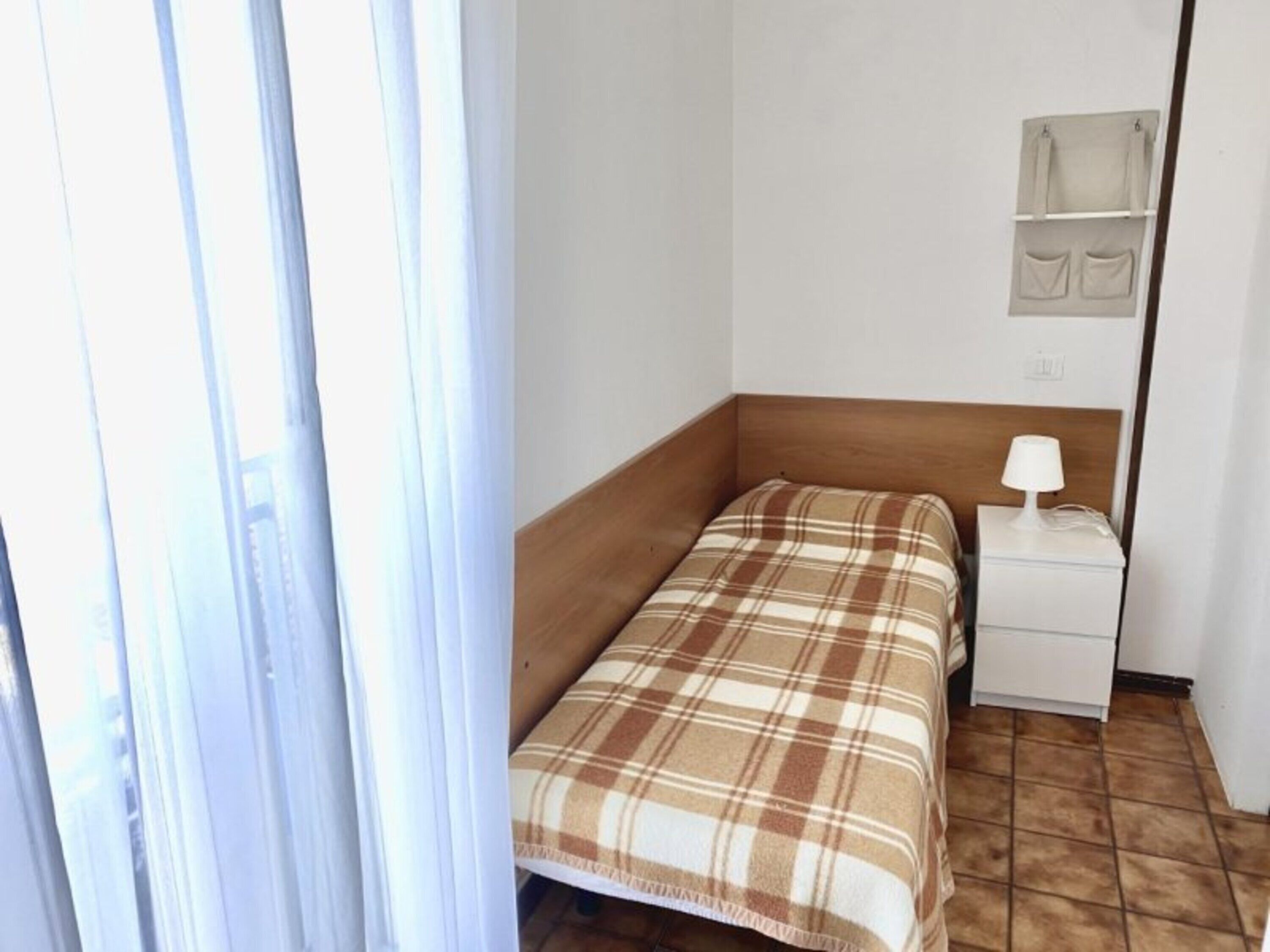 A small hotel room with a bed, a nightstand, a lamp, and a wall-mounted shelf.