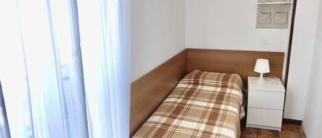 A small hotel room with a bed, a nightstand, a lamp, and a wall-mounted shelf.