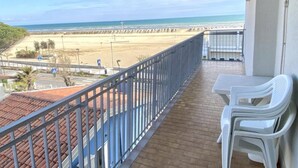 Ein Balkon mit Blick auf den Strand, einem Geländer und zwei weißen Plastikstühlen.