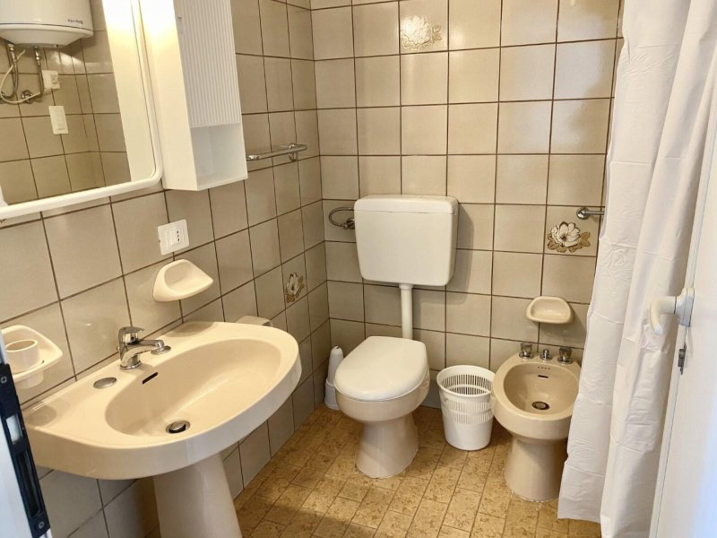 Une salle de bain équipée d’un lavabo, de toilettes, d’un bidet et d’un rideau de douche.