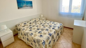 Ein Schlafzimmer mit einem Bett, einem Nachttisch, einem Schreibtisch, einem Fenster und einem Bild an der Wand.