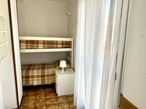 Pieni, yhden huoneen kokoinen majoituspaikka, jossa on kerrossänky, yöpöytä lampulla ja laattalattia.
