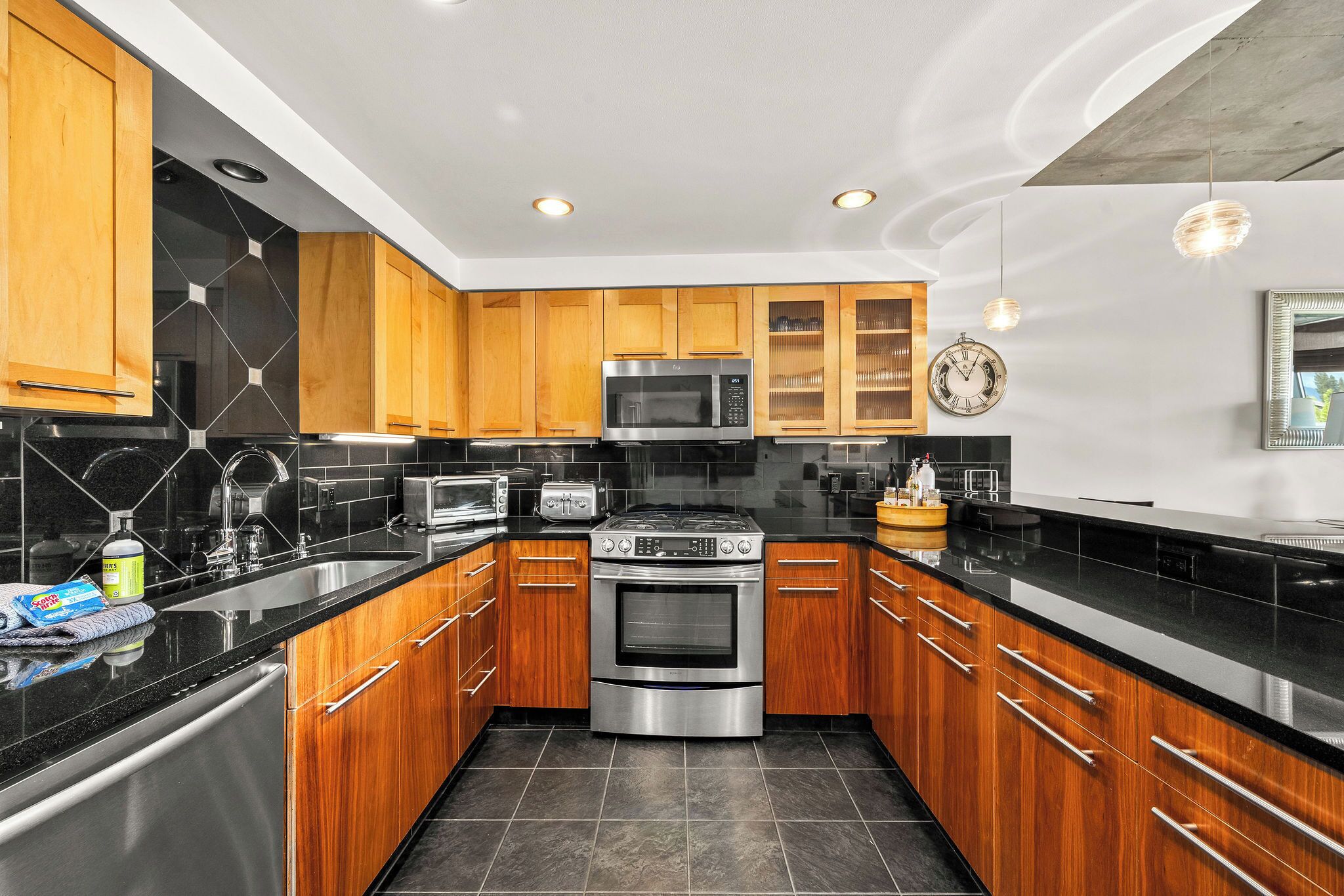 A modern kitchen with wooden cabinets, stainless steel appliances, and black countertops.