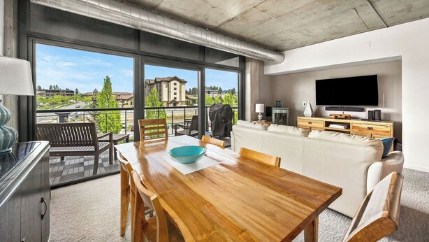 Un salon moderne avec une table à manger en bois, un canapé, un téléviseur à écran plat et de grandes fenêtres donnant sur l’extérieur.