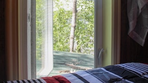 A bed with a striped bedspread, a window with a sheer curtain, and a view of trees outside. - Escape to Lake Metigoshe This Summer (Bottineau)