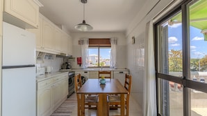 Una cocina con armarios blancos, una mesa de comedor con sillas, un ventanal con cortinas y vistas al exterior.