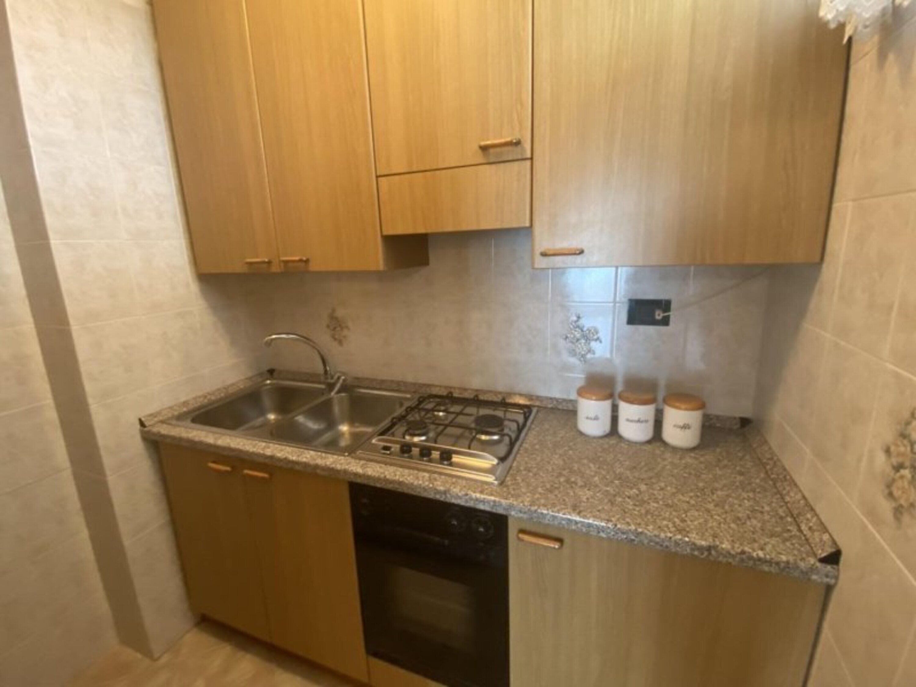 Une cuisine avec des meubles de rangement en bois, un évier en acier inoxydable, une cuisinière à gaz et trois pots blancs posés sur le plan de travail.