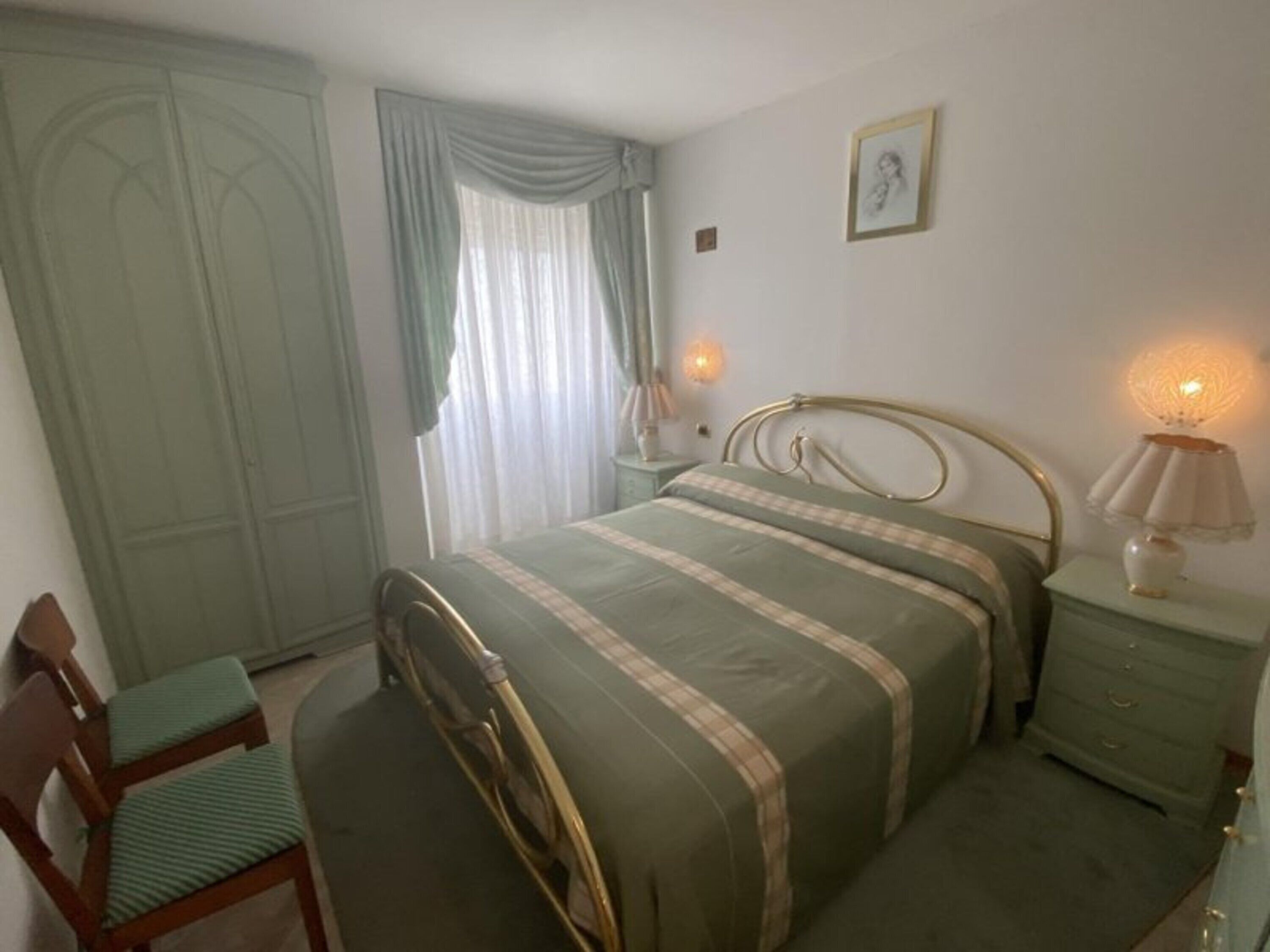 Une chambre à coucher comprenant un lit, une table de chevet, une chaise, une armoire et une fenêtre avec des rideaux.