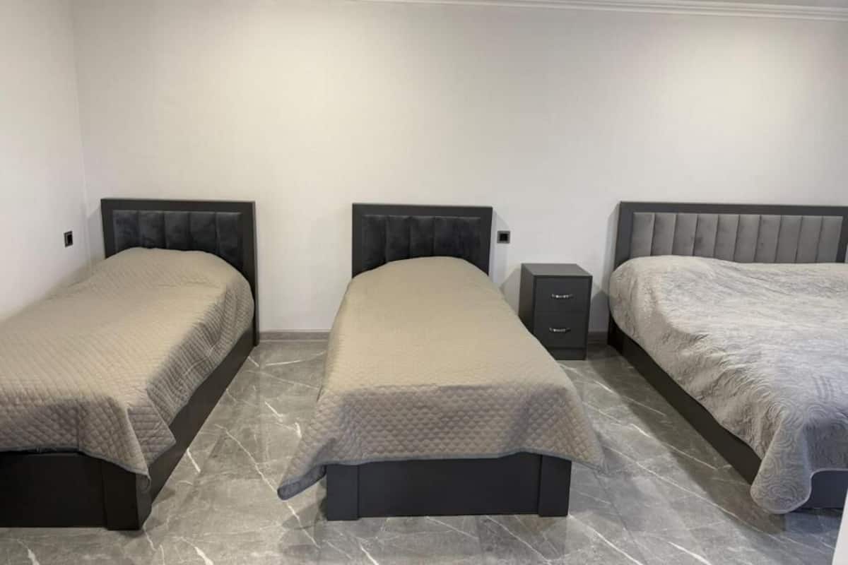 Un dormitorio con tres camas, una mesita de noche y suelo de mármol.