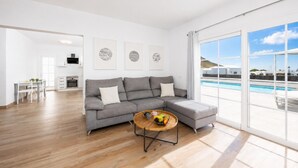 A modern living room with a grey sectional sofa, a dining area, and a view of a swimming pool. - Villa Yaiza Secret 2 (Yaiza)