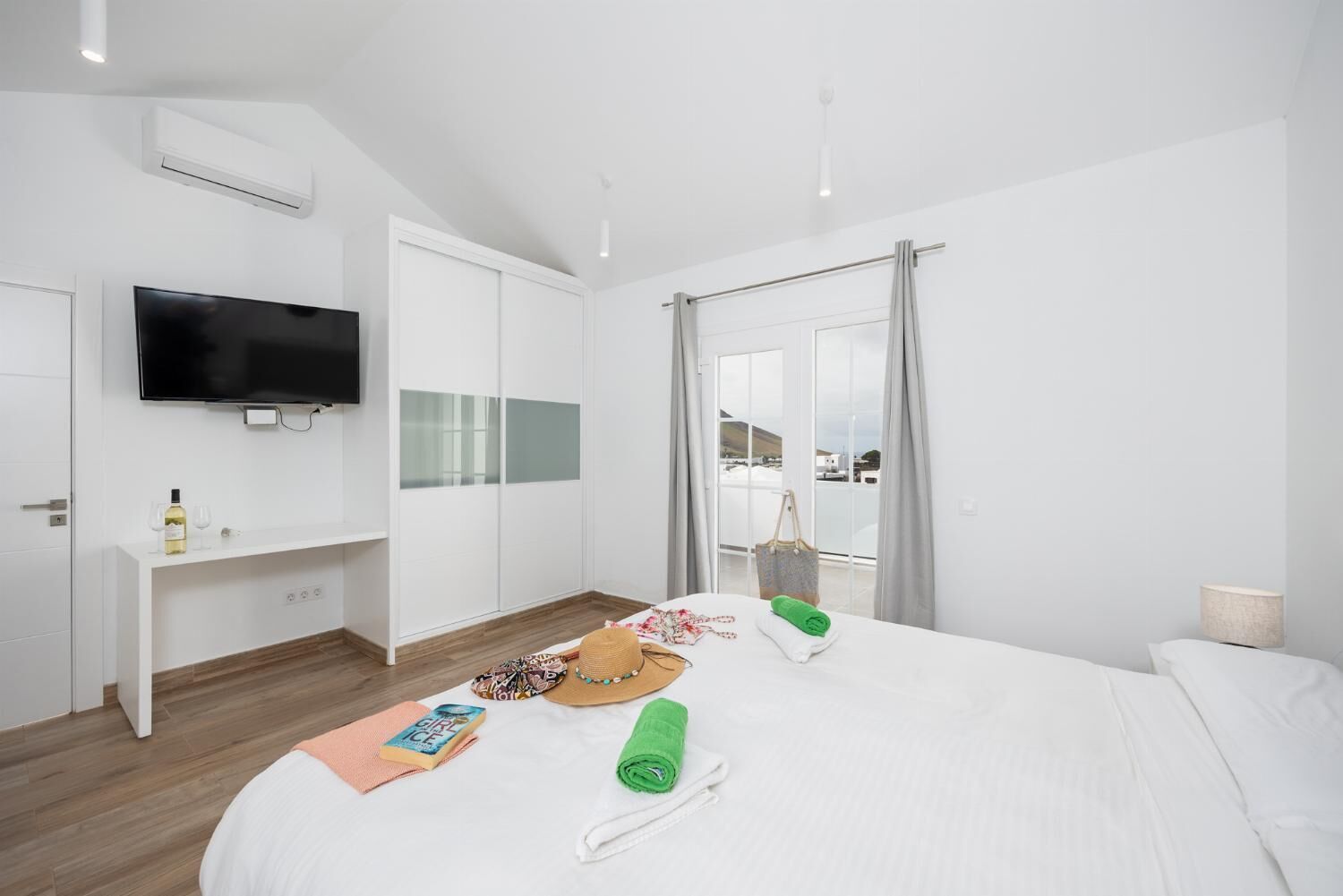 Una camera d'albergo moderna con un letto grande, una TV a schermo piatto montata a parete, un armadio bianco e un balcone con vista.