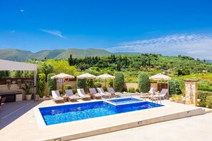 Un espace piscine agrémenté de chaises longues et de parasols, entouré de verdure et de collines.