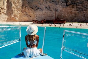 Eine Person sitzt in einem Boot und blickt auf einen Strand und steile Klippen.