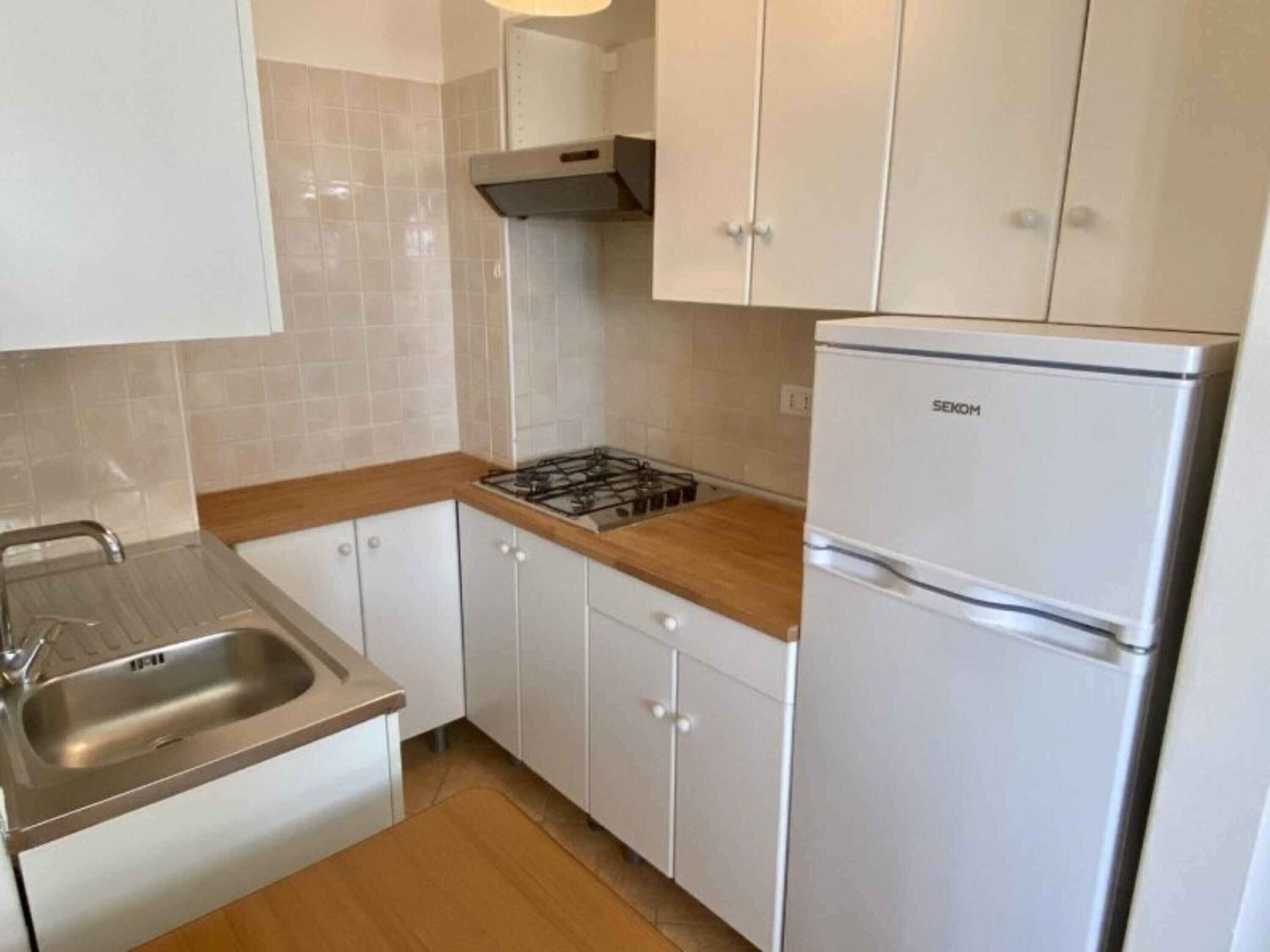 Una cocina con armarios blancos, un lavamanos de acero inoxidable, una estufa a gas y un refrigerador blanco.