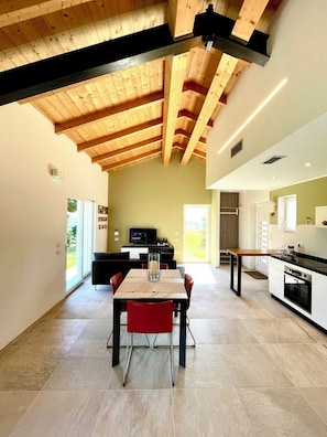 A modern kitchen with a dining area, wooden ceiling beams, and a large window. - Wellness hillside house in Le Marche (Recanati)