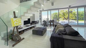 A modern living room with a glass staircase, a sofa, a TV, and a view of greenery outside. - Beachfront villa with jacuzzi in Senigallia (Marzocca)