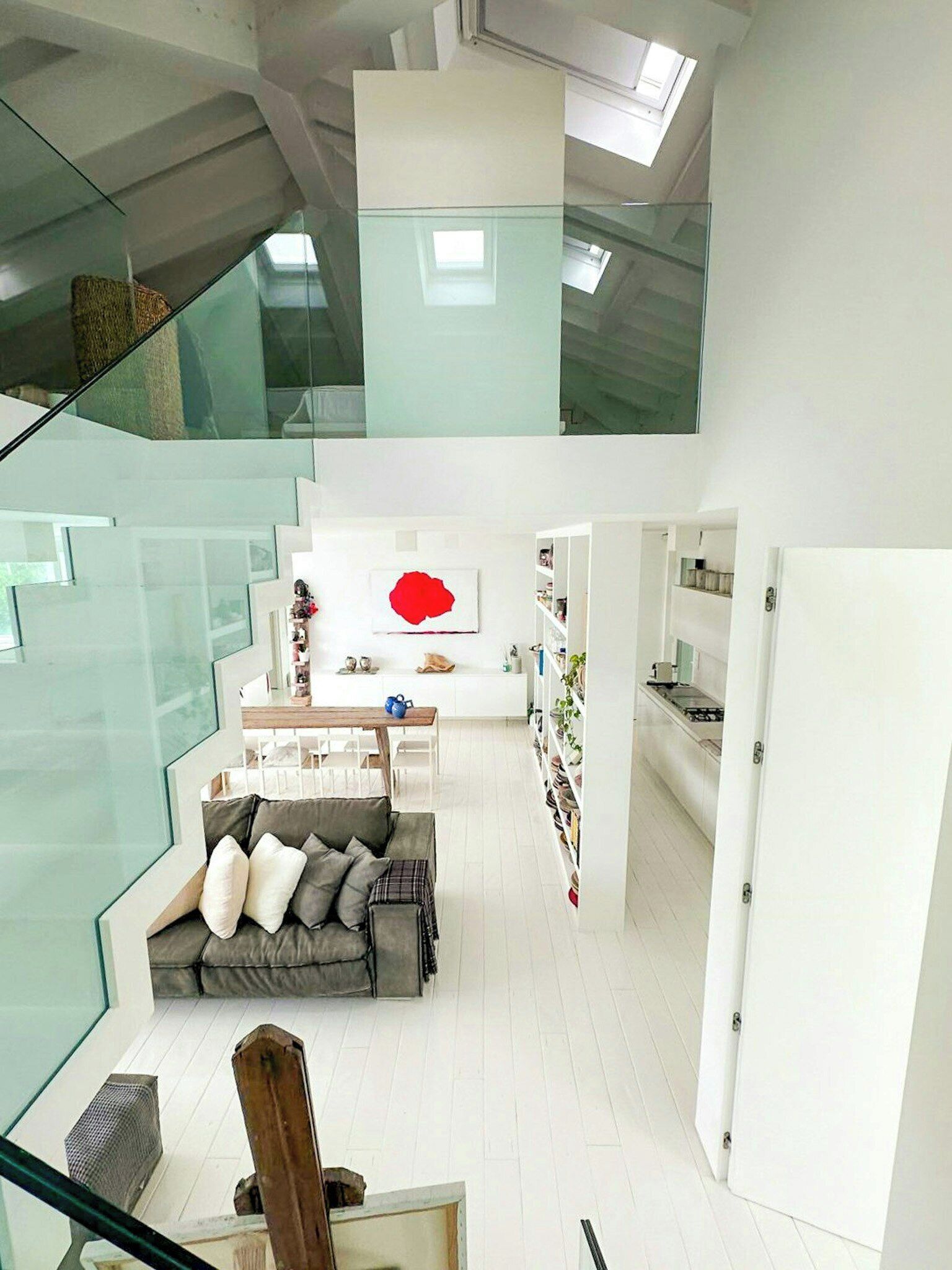 Un interior moderno con una escalera de cristal, una sala de estar con sofá, una mesa de comedor y una zona de cocina.