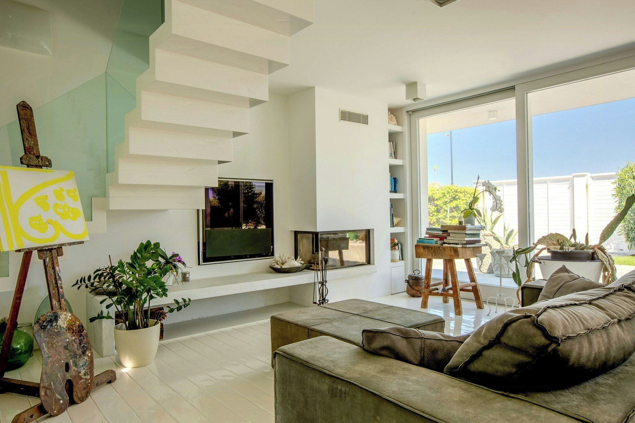 A modern living room with a flat-screen TV, a fireplace, a staircase, and a large window.