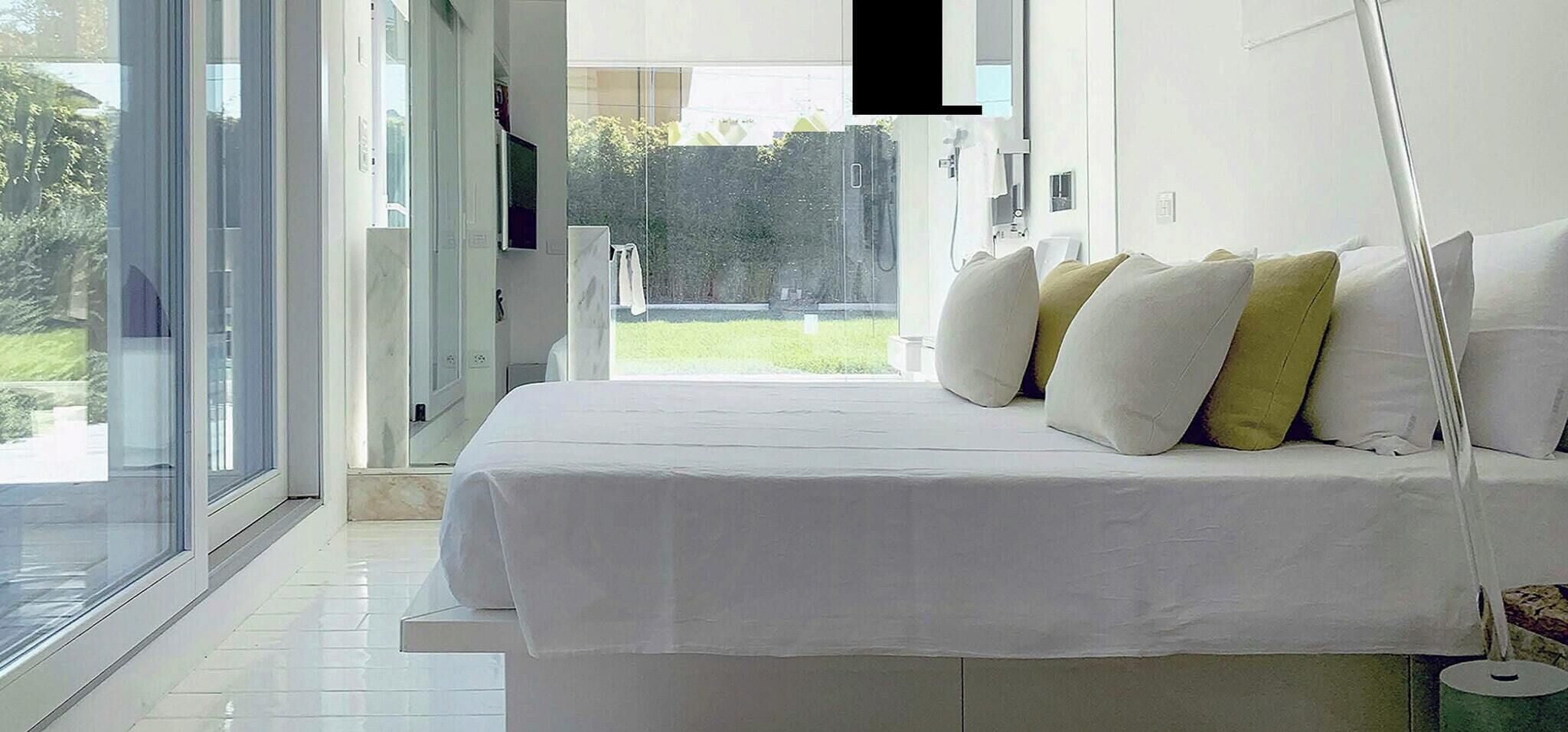 Une chambre moderne avec une grande fenêtre, un lit avec une literie et des oreillers blancs, et une table de chevet.