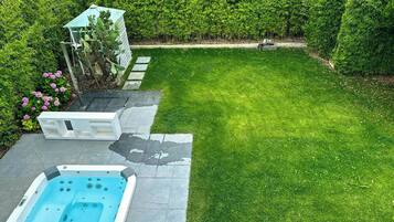 Un giardino sul retro con una vasca idromassaggio, un piccolo deposito e un prato curato.