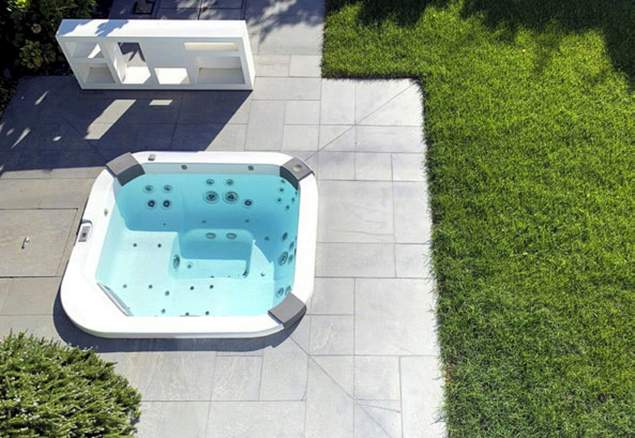 Un jacuzzi en un patio con baldosas y un césped cercano.