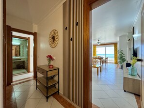 Ein Flur, der in einen Essbereich mit Meerblick führt, mit einem Holzschrank, einer Vase mit Blumen und einem Spiegel an der Wand.
