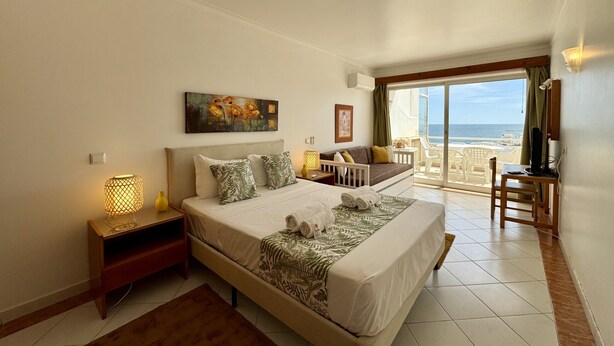 A bedroom with a bed, bedside tables, a painting, a sofa, a TV, and a balcony with a view. - Albufeira Amazing View 2 by Homing (Albufeira)
