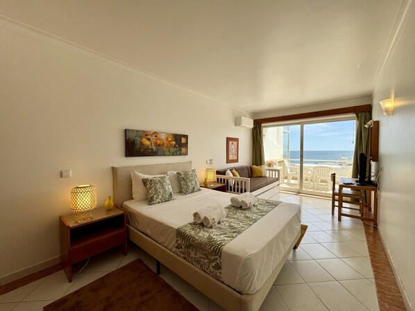 Ein Schlafzimmer mit Bett, Nachttischen, einem Gemälde, einem Sofa, einem Fernseher und einem Balkon mit Blick.