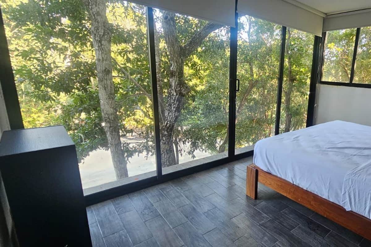 A bedroom with a large window, a bed, and a wooden floor.