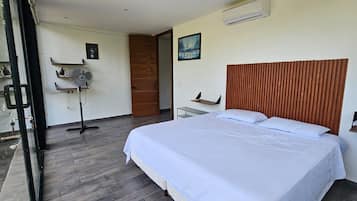 Un dormitorio con cama, ventilador, puerta de madera y ventana.